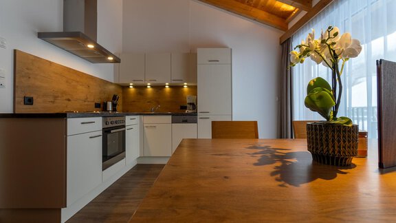 A modern kitchen with wooden and white elements. On the table stands a decorative flower pot. - Anraitl Appartements Sölden - Sölden