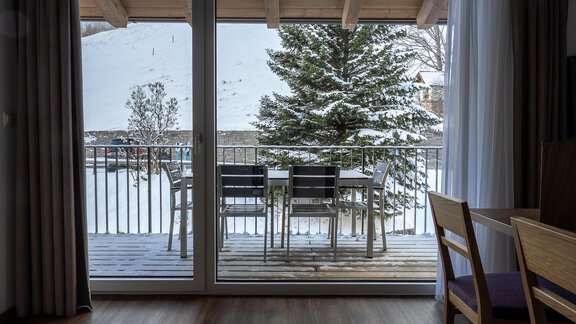 A cozy balcony with a table and chairs, overlooking a snowy landscape. In the background, there is a green tree and a slightly cloudy sky. - Anraitl Appartements Sölden - Sölden