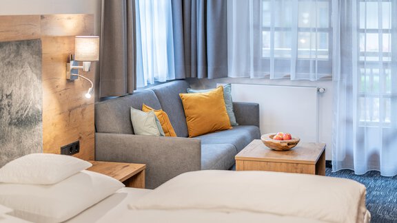 A bright and modern hotel room with a comfortable sofa and colorful cushions. The room has large windows that let in plenty of daylight. - Apart Hotel Garni Alt Kaisers - Sölden