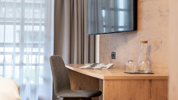 A modern desk with a chair and a television on the wall. Bright curtains let natural light into the room. - Apart Hotel Garni Alt Kaisers - Sölden