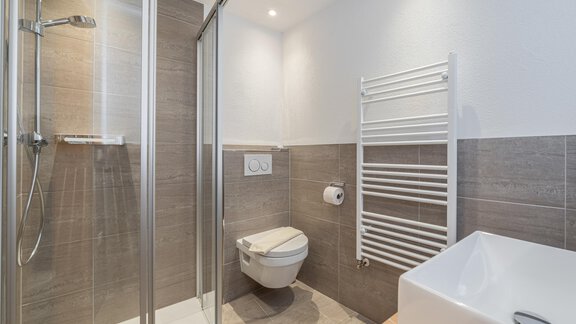 A modern bathroom with a shower, a WC, and a sink. The walls are in neutral colors, and there is a towel warmer. - Apart Hotel Garni Alt Kaisers - Sölden