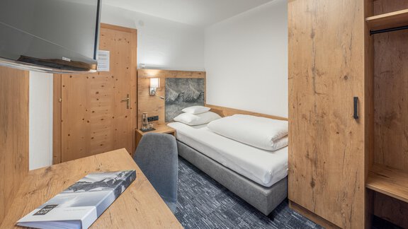 A cozy hotel room with wooden furniture and a single bed. The room is bright and modernly furnished, with a desk and a television. - Apart Hotel Garni Alt Kaisers - Sölden