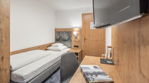 A cozy room with wood paneling and a single bed. A television and a small desk are also available. - Apart Hotel Garni Alt Kaisers - Sölden