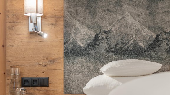 A modern bedroom with a printed mural of mountains and a warm wooden wall. Next to the bed are pillows and a discreet wall lamp. - Apart Hotel Garni Alt Kaisers - Sölden