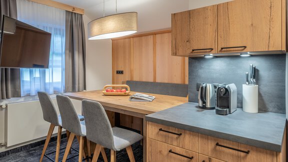A modern kitchen with wooden cabinets and a large wooden countertop. A dining table with chairs and a small fruit bowl are also visible. - Apart Hotel Garni Alt Kaisers - Sölden