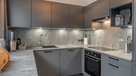 A modern kitchen with gray cabinets and an elegant countertop. The lighting creates a pleasant atmosphere. - Apart Hotel Garni Alt Kaisers - Sölden
