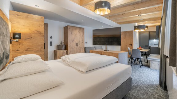 A modern hotel room with a large bed and wooden furniture. The room is bright and cozy, with a small dining area. - Apart Hotel Garni Alt Kaisers - Sölden