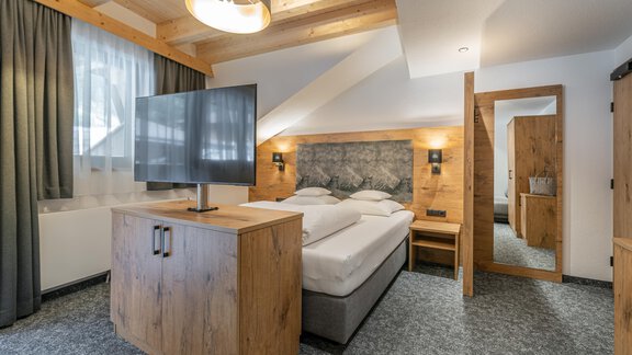 A modern bedroom with a double bed and a flat-screen TV. The cozy atmosphere is accentuated by wooden elements and soft lighting. - Apart Hotel Garni Alt Kaisers - Sölden