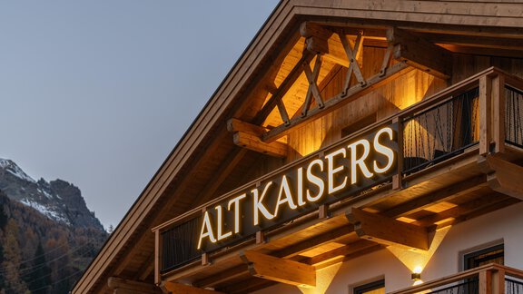 A beautifully designed wooden building named "ALT KAISERS". The façade is illuminated with warm light and the surroundings feature a mountain landscape. - Apart Hotel Garni Alt Kaisers - Sölden
