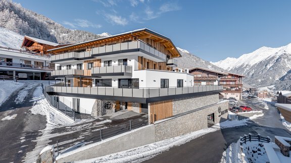 A modern building in the Alps, surrounded by snow-capped mountains. The architecture combines wood and concrete with large windows for plenty of daylight. - Apart Natur - Sölden
