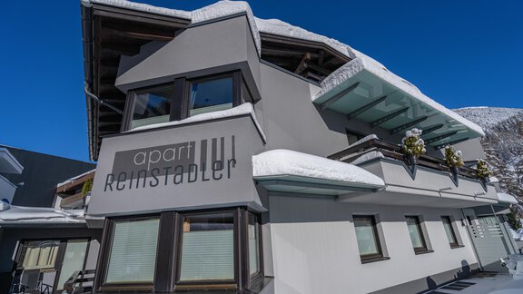 Ein modernes Gebäude mit dem Namen "apart Reinstadler" in einem schneebedeckten Gebiet. Der klare blaue Himmel ergänzt die winterliche Atmosphäre. - Apart Reinstadler - Sölden