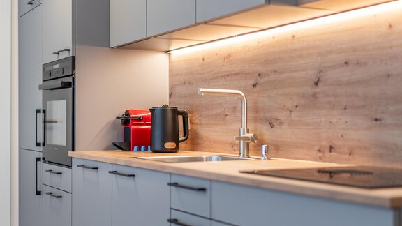 A modern kitchen with gray cabinets and wooden details. On the countertop, there is a kettle and a coffee maker. - Apart Sonnenbichl - Sölden
