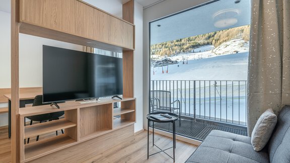 A modern living room with a large television and a comfortable sofa. A beautiful winter landscape with snow can be seen through the windows. - Apart Sonnenbichl - Sölden