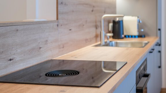 Modern kitchen with a smooth wood countertop and an integrated cooktop. In the background, a sink and small kitchen appliances can be seen. - Apart Sonnenbichl - Sölden
