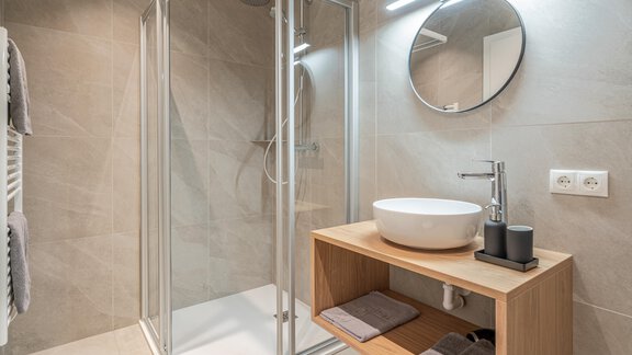 A modern bathroom with a clear shower cubicle and an elegant sink. The wooden cabinet provides space for towels and toiletries. - Apart Sonnenbichl - Sölden