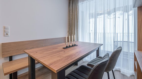 An elegant dining area with a wooden table and a bench. Curtains let in soft light and create a cozy atmosphere. - Apart Sonnenbichl - Sölden