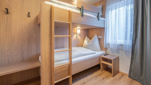 A modern room with a wooden bunk bed and a small nightstand. The windows let in a lot of light and the walls are brightly designed. - Apart Sonnenbichl - Sölden