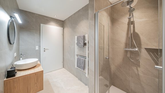 A modern bathroom with a walk-in shower and a wooden sink. The walls are painted in a neutral gray and the lighting is bright and inviting. - Apart Sonnenbichl - Sölden