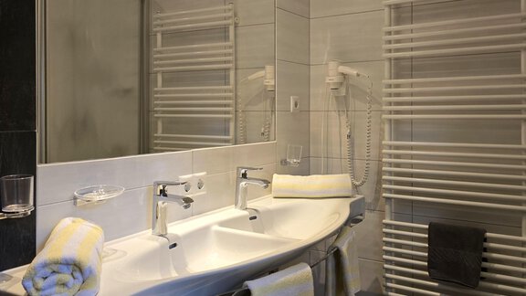 A modern bathroom with two sinks and a large mirror. The walls are light and the furnishings are elegant and functional. - Apart Tyrolis - Sölden