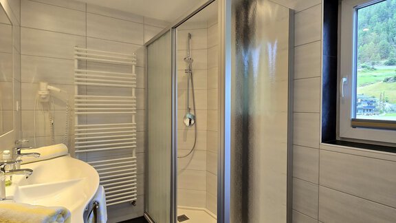 A modern bathroom with a shower and a large window. The walls are tiled in light colors, and there are towels and a towel rack. - Apart Tyrolis - Sölden