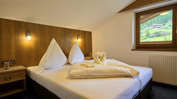 A cozy bedroom with a large double bed. The walls are made of wood, and there is a window view of nature. - Apart Tyrolis - Sölden