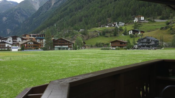 A picturesque mountain landscape with green meadows and traditional chalets. In the background, high mountains and a cloudy sky can be seen. - Apart Tyrolis - Sölden