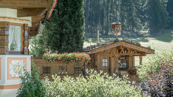 A picturesque wooden house surrounded by green trees and colorful flowers. The idyllic surroundings convey a sense of tranquility and connection to nature. - Apart Wiesengrund - Sölden