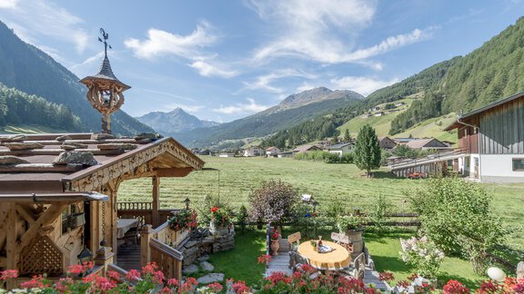 A picturesque landscape with green meadows and mountains in the background. In the foreground, colorful flowers are blooming, and a wooden house complements the idyllic scenery. - Apart Wiesengrund - Sölden
