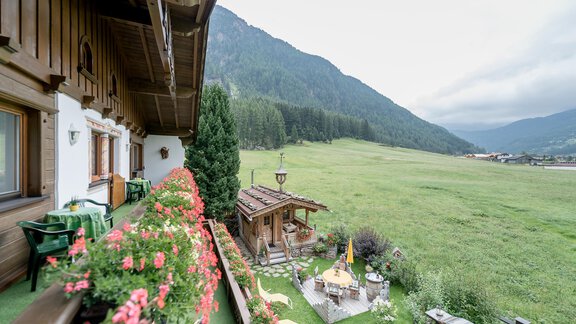 A picturesque view from a balcony with flowers and a look at a green meadow and mountains in the background. The sky is cloudy and there is a small pavilion in the garden. - Apart Wiesengrund - Sölden