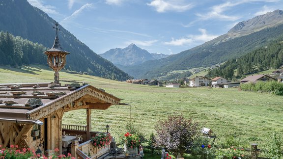 A picturesque mountain landscape with a wooden house and blooming flowers. In the background, majestic mountains and a blue sky can be seen. - Apart Wiesengrund - Sölden