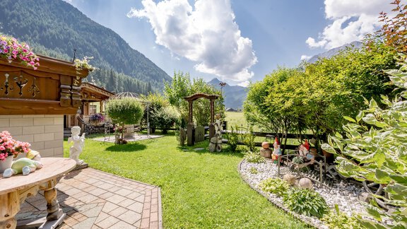 A beautiful garden with green grass and colorful flowers. In the background, you can see mountains under a blue sky with some clouds. - Apart Wiesengrund - Sölden