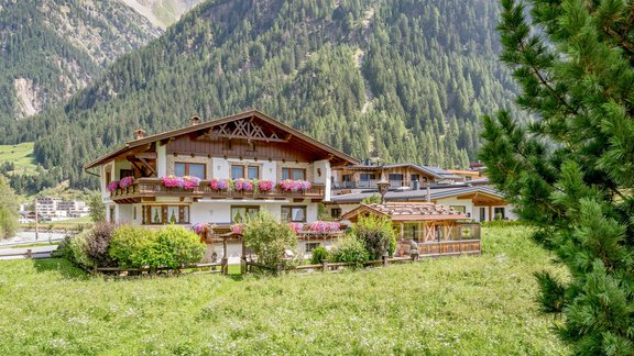 A picturesque chalet surrounded by green meadows and majestic mountains. Colorful flowers adorn the windows, creating a cozy atmosphere. - Apart Wiesengrund - Sölden