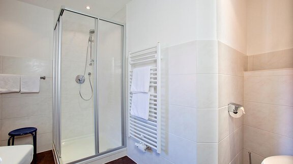 A modern bathroom with a shower and white tiles. There is a towel rack and a toilet in the room. - Appartement Alpin - Sölden