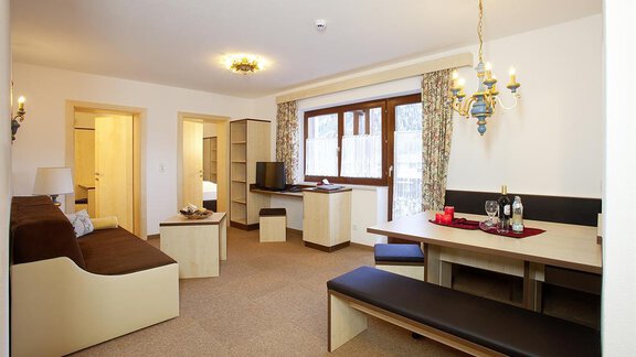 A cozy living space with a sofa, a dining area, and a large window. The decor is modern and brightly designed. - Appartement Alpin - Sölden