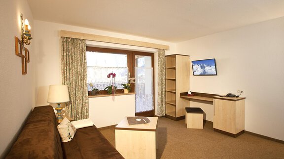 A cozy living space with a sofa, a table, and a television.  
Large windows let in plenty of light and offer a view outside. - Appartement Alpin - Sölden