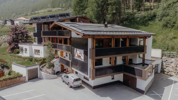 A modern building in a mountainous area, surrounded by trees. There are parking options and an inviting entrance area. - Appartement Alpin - Sölden