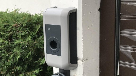 A charging station for electric cars, installed on a wall. Nearby, green plants are visible. - Appartement Alpin - Sölden