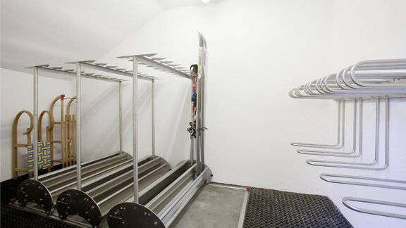 A modern ski room with metal shelves for skis and snowboards. The walls are white and the floor is covered with non-slip material. - Appartement Alpin - Sölden