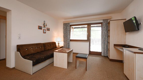 A cozy living room with a sofa, a table, and a television. Large windows let in plenty of light. - Appartement Alpin - Sölden