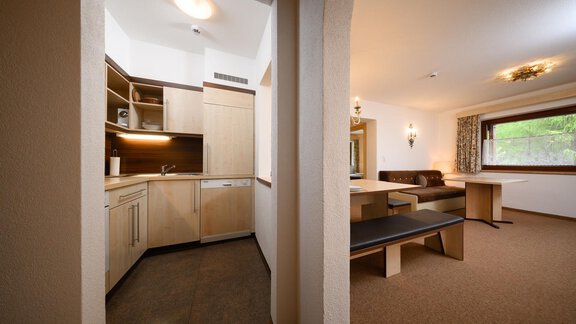 A modern kitchen with wooden cabinets and plenty of space. The adjacent living area is cozily furnished and features large windows. - Appartement Alpin - Sölden
