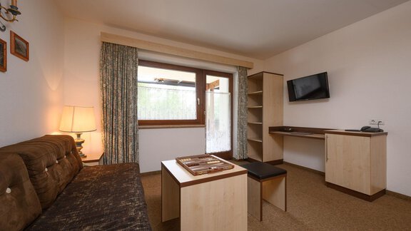 A cozy living room with a sofa, a table, and a television. The room has large windows that let in natural light. - Appartement Alpin - Sölden