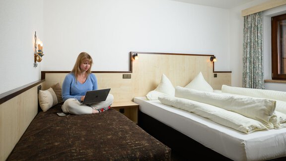 A cozy room with a bed and a sofa. A person is sitting at the computer and working. - Appartement Alpin - Sölden