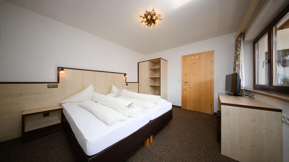 A modern bedroom with a double bed and light wooden furniture. Next to the bed are a wardrobe and a television, and the room has windows that let in plenty of daylight. - Appartement Alpin - Sölden