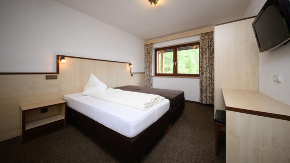 A simple bedroom with two beds and a window that offers a view of nature. The decor is modern and minimalistic. - Appartement Alpin - Sölden