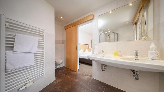 A modern bathroom with bright fixtures and large mirrors. The walls are light and there is a shower as well as towel holders. - Appartement Alpin - Sölden