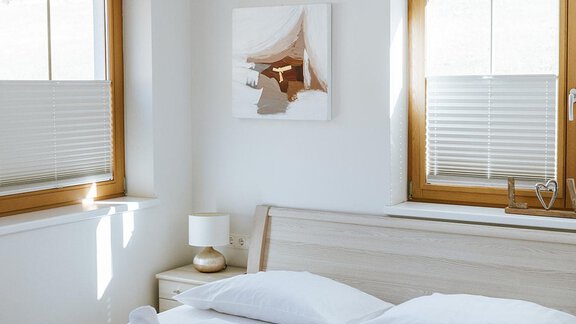 A bright bedroom with a large bed and white bed sheets. There are windows with blinds and a modern ceiling lamp. - Appartement Bergbach Sölden - Sölden