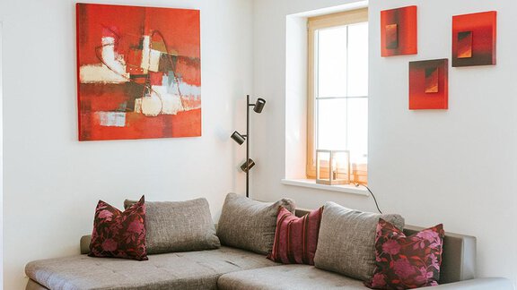 A cozy living room with a gray couch and colorful cushions. Some colorful pictures hang on the wall, and the room has a modern, inviting style. - Appartement Bergbach Sölden - Sölden