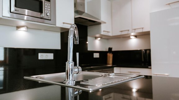 A modern kitchen with a sleek sink and a smooth countertop. In the background, kitchen cabinets and a microwave are visible. - Appartement Bergbach Sölden - Sölden