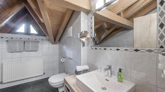A modern bathroom with a wooden ceiling and white tiles. The wash area is equipped with an elegant sink and a large mirror. - Appartement Cristallo - Sölden