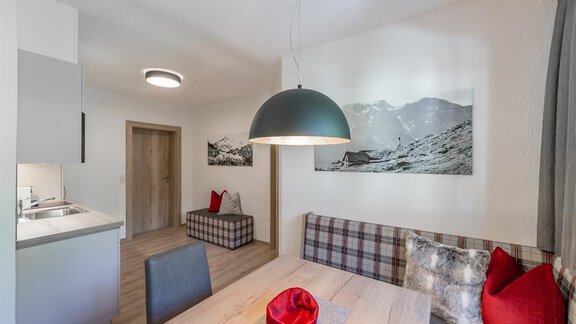 A modern dining room with a large wooden table and comfortable seating. The walls are decorated with stylish photos and a large chandelier. - Appartement Cristallo - Sölden
